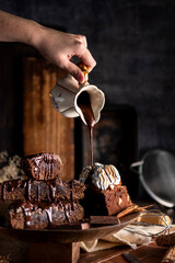 Chocolate brownie cake with cream sauce on table with chocolate bar ingredients and kitchen utensils