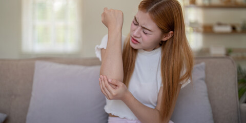 Young woman feeling elbow pain while sitting on sofa at home