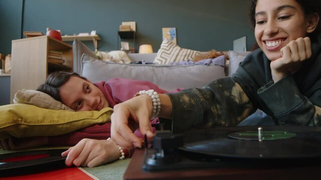 Medium shot of Caucasian teenage girl with cerebral palsy and her Biracial female friend chatting and listening to music on vinyl record player at home