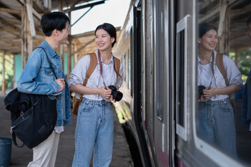 Happy young Asian couple carrying backpacks and cameras preparing to wait for the train at the...
