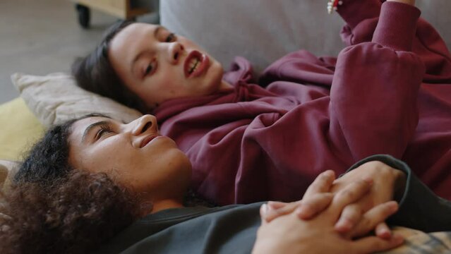 Caucasian teenage girl with cerebral palsy and her Biracial female best friend lying on couch next to each other and talking
