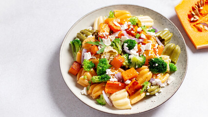 Autumn pasta salad with roasted pumpkin, broccoli, feta cheese on bright light background, fall...