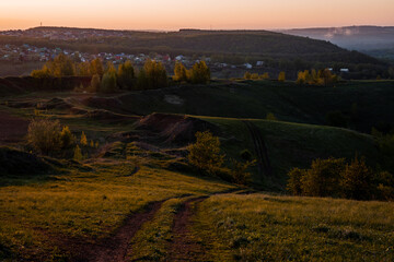 Dirt road winding through grassy hillside at sunset