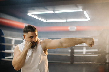 A male boxer is boxing with a shadow on the background of a boxing ring. A boxer practices his punches in a boxing studio.