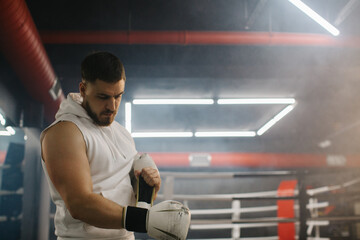 A male boxer puts on gloves on the background of a ring in a boxing club.