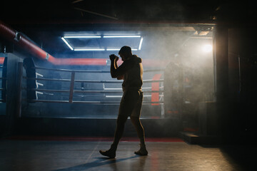 A male boxer is boxing with a shadow on the background of a boxing ring. A boxer practices his...