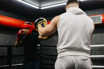 A teenager wearing a red protective helmet and gloves trains in a boxing ring with a coach.