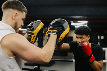A male trainer helps a teenage boxer with striking techniques in a boxing ring.