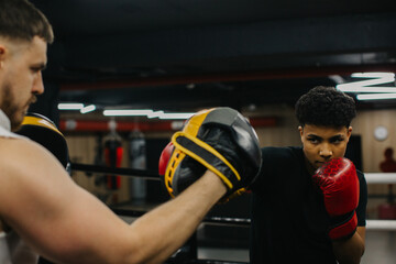 A young boxer practices punches with a trainer in a boxing studio.