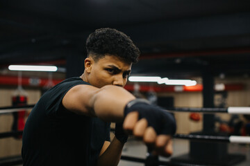 A focused young boxer practices his punches. Sporty young man training in boxing gym.
