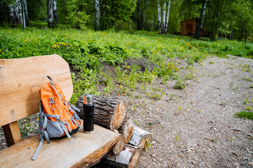A wooden bench in a natural landscape with a backpack and thermos