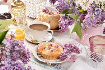Sweet tartlet and a cup of coffee on the table decorated with lilac blossoms