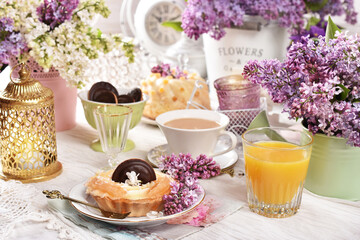 Sweet tartlet and a cup of coffee on the table decorated with lilac blossoms