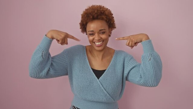 Stunning african american woman in sweater beams with self-pride, playfully pointing at herself. exuding confidence and joy, she stands against a pink background.