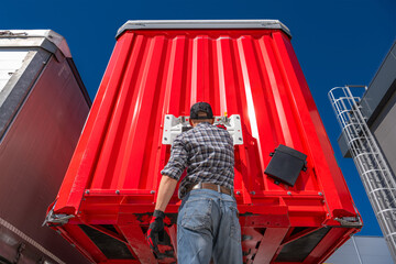 Trucker performing maintenance on the rear of a red semi trailer
