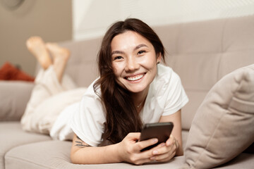 Happy Young Woman Relaxing On Couch With Smartphone, Enjoying Leisure Time At Home, Cheerful...