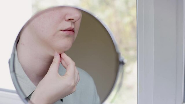 double chin in a caucasian woman. Woman pinching fat on chin and looking at mirror close up