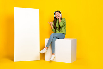 Full size photo of young excited girl indicate finger poster suggest promotion electronic web isolated over yellow color background