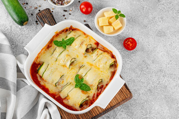 Baked zucchini rolls with ground meat, tomato sauce and cheese in a white baking dish on a gray...