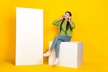 Full body photo of young girl listen radio earphones meloman mp3 promo sit podium isolated over yellow color background