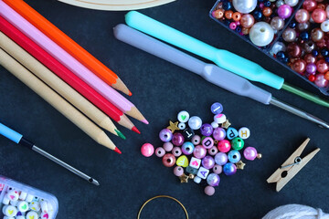 Colorful beads, coloring pencils, glitter, needles, string, hoop, tape and scissors on dark...