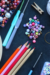 Colorful beads, coloring pencils, glitter, needles, string, hoop, tape and scissors on dark...
