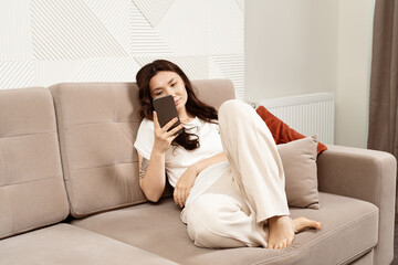 Relaxed Young Woman Using Smartphone On Couch, Modern Home Decor Background, Leisure Time At Home, Contemporary Lifestyle
