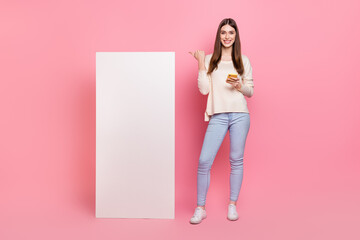 Full length body size view of beautiful trendy girl using device showing copy space ad isolated over pink pastel color background