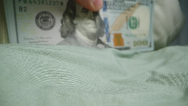 Large Stack of One Hundred Dollar Bills Under a Pillow on the Bed, Man's Hand Takes Them. Macro Slider.
