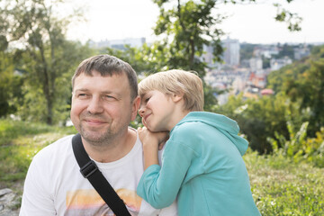 Portrait of a happy dad and son. A cute boy of 6-7 years old is lying on his dad s shoulder. Walk in the park. Father's Day, Son's Day. Tender relationships in the family