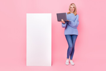 Full length photo of senior blond lady hold laptop near promo wear pullover jeans sneakers isolated on pink background