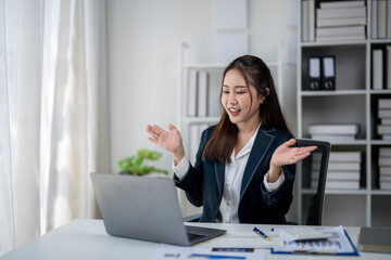 A woman in a business suit is sitting at a desk with a laptop open. She is smiling and she is happy