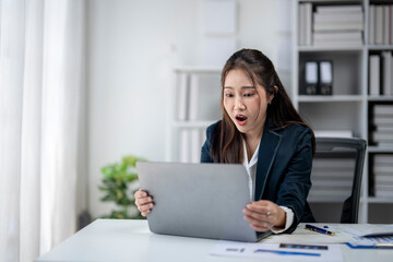 A woman in a business suit is looking at a laptop screen with a surprised expression on her face