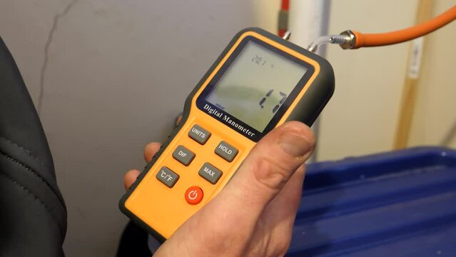 Gas engineer measuring pressure holding in his hand portable digital manometer connected to domestic piping or pipework, close up shot.