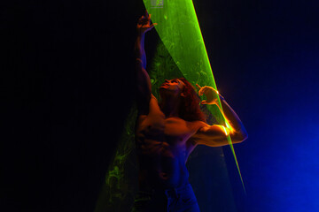 Sporty handsome muscular man portrait under colorful illumination, laser light