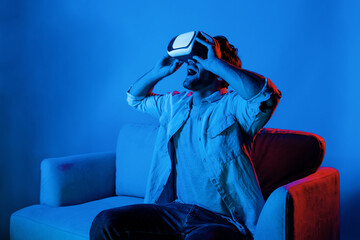 Happy man sitting at sofa while wearing VR goggle to watch funny movie. Caucasian person relaxed...