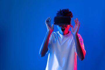 Surprised young African American looking through VR holding interesting object hologram on pink...