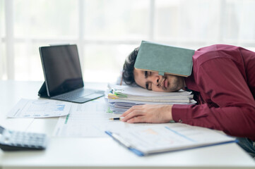 A man is sleeping on his desk with a book on his head