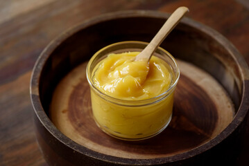 Ghee butter in glass jar with wooden spoon on wooden table with blurred background.