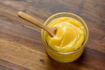 Ghee butter in glass jar with wooden spoon on wooden table with blurred background.