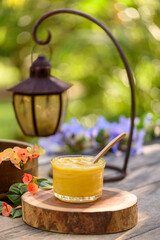 Ghee butter in a glass container on a wooden table, with flowers and leaves in the blurred background.