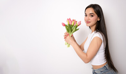Young brunette woman posing isolated over white wall background holding flowers