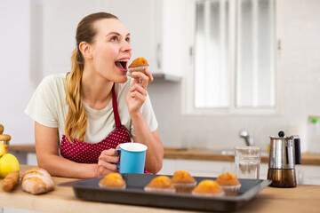 Woman in apron tasting freshly baked sweet cupcakes in kitchen