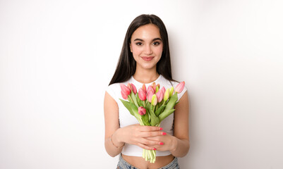 Young brunette woman posing isolated over white wall background holding flowers