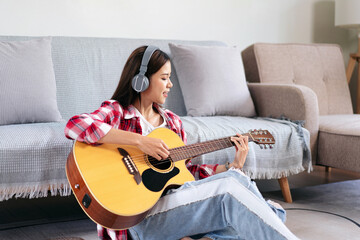 Young woman is playing guitar and singing the song while wearing headphone to listening music and...