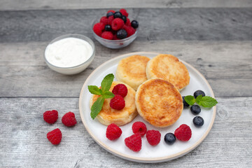 Cottage cheese pancake or syrniki with fresh raspberries and blueberry on dark wooden table.  Sweet breakfast or lunch, tasty dessert. 