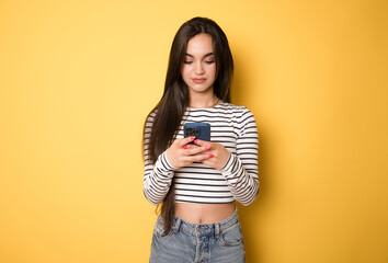 Portrait of Beautiful young brunette woman holding a phone on yellow background