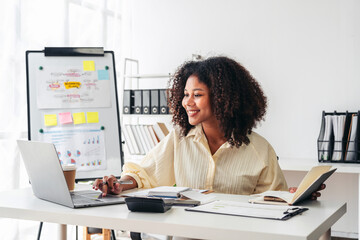 A woman is sitting at a desk with a laptop and a book