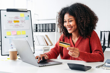 A woman is smiling while using a laptop and holding a credit card