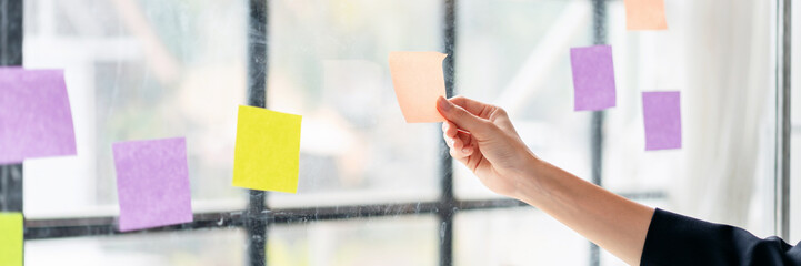 A hand is holding a yellow and purple sticky note